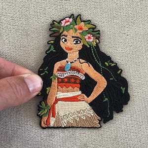May include: Embroidered patch featuring a Polynesian woman with long black hair, a floral crown, and a traditional outfit. The patch has a detailed design with vibrant colors, including red, brown, and green, and is likely for clothing or accessories.