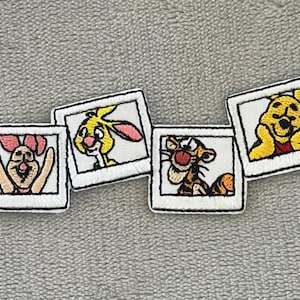 May include: Embroidered patches featuring characters from Winnie the Pooh. The patches include Owl, Piglet, Rabbit, Tigger, Winnie the Pooh, and Eeyore, each in a white framed square. The patches are on a gray surface.