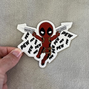 May include: A red and black Deadpool patch with the word "PEW" repeated around the character. The patch features Deadpool holding two silver guns. The patch is white with a black border.