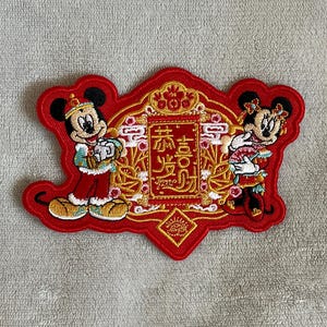 May include: Red embroidered patch featuring Mickey and Minnie Mouse dressed in traditional Chinese clothing. The patch has gold accents and the Chinese characters "福" and "喜" which mean "good fortune" and "joy".
