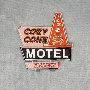 以下が含まれることがあります： COZY CONE MOTELおよびNO VACANCYという文字が入ったモーテルの看板デザインの刺繍ワッペン。オレンジ色の三角コーンのグラフィックに、眠っている車のアイコンと、白い糸で垂直に繰り返されたZの文字がデザインされています。