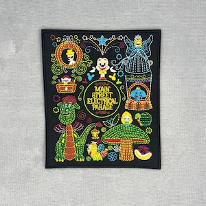May include: A rectangular black embroidered patch featuring colorful thread designs of characters and the text Main Street Electrical Parade. The imagery includes a green dragon, a mushroom, a carriage, and various parade floats in vibrant hues.