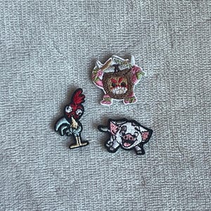 May include: Three embroidered patches featuring characters from a popular animated film. One patch depicts a rooster with red and blue details. Another shows a pig with pink and black accents. The third patch is a coconut character with floral details.