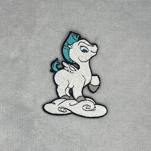 May include: An embroidered patch featuring a white winged horse with a teal mane and tail, standing on a white cloud. The design is outlined in black thread, showcasing a cartoon-style creature with small wings and grey hooves on a textured surface.