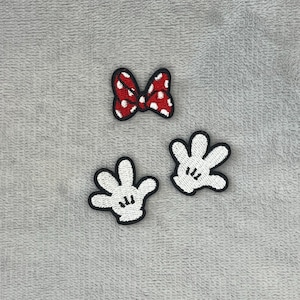 Può includere: Tre toppe ricamate: un fiocco rosso a pois bianchi con bordo nero e due guanti bianchi con contorni neri. Le toppe sono probabilmente per abbigliamento o progetti artigianali.