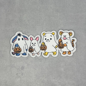 May include: An embroidered patch featuring four cartoon characters dressed in white ghost costumes for Halloween. Each character holds a small orange jack-o'-lantern bucket. The characters are arranged in a row, showcasing distinct ears and tails.