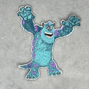 May include: Embroidered patch featuring Sulley from Monsters, Inc. The patch depicts the blue monster with purple spots, large hands, and a wide, toothy grin. The patch is designed with a white border and is likely for application on clothing or accessories.