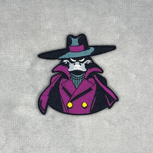 Pode incluir: Um emblema bordado apresentando uma personagem de desenho animado usando um chapéu de aba larga com uma faixa azul-petróleo, um sobretudo roxo de gola alta com lapelas pretas e dois botões amarelos. A personagem tem um rosto branco e bico.