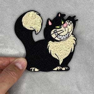 Puede incluir: Parche bordado con un gato negro sonriente con una gran sonrisa, nariz rosa y ojos verdes. El gato tiene el pecho y la punta de la cola de color crema. El parche es para ropa o accesorios.