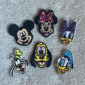 Op de afbeelding: Geborduurde patches met populaire Disney-personages: Mickey Mouse, Minnie Mouse, Katrien Duck, Donald Duck, Goofy en Pluto. Elke patch toont levendige kleuren en gedetailleerde steken, perfect om kleding of accessoires te personaliseren.