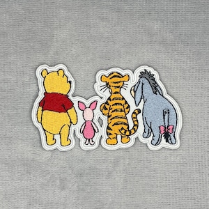 May include: An embroidered patch featuring the backs of four cartoon characters: a yellow bear in a red shirt, a small pink piglet, an orange tiger with black stripes, and a blue donkey with a pink bow tied to its tail, all on a grey background.