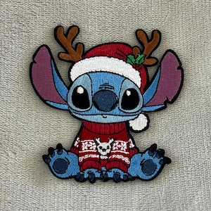 Op de afbeelding: Geborduurde patch met het personage Stitch, gekleed in een kersttrui en een kerstmuts met geweien. De patch is blauw, rood, bruin en wit, perfect voor kerstknutselwerkjes en kleding.