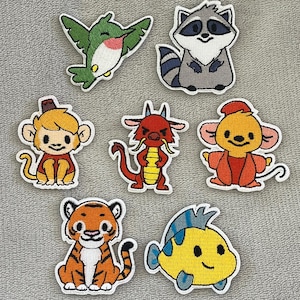 Op de afbeelding: Een verzameling geborduurde patches met verschillende cartoon dieren. Inclusief een kolibrie, wasbeer, aap, draak, muis, tijger en vis. Elke patch heeft een witte rand en is felgekleurd.