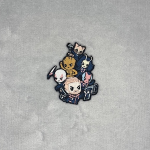 Op de afbeelding: Een geborduurde patch met een groep gestileerde, chibi-stijl personages uit een sciencefictionfilm, waaronder een bruine boomachtige figuur, een wasbeer en verschillende humanoïden in donkerblauwe uniformen, allemaal met zwarte omlijningen.
