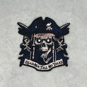 May include: Embroidered patch featuring a skull wearing a pirate hat with the text "Dead Men Tell No Tales." The patch is primarily navy blue with white and pink accents. The skull has glowing eyes and is surrounded by details.