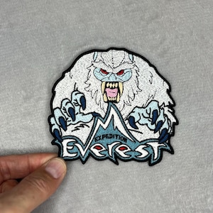 May include: Embroidered patch depicting a white yeti with red eyes and a snarling expression. The patch features the text "Expedition Everest" in blue and white, with a mountain graphic.