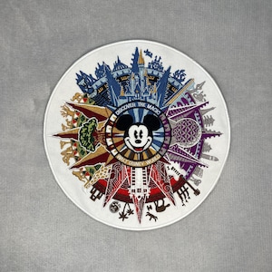 Puede incluir: Un parche bordado circular que presenta una cabeza de Mickey Mouse central rodeada por un diseño radial colorido de puntos de referencia de Walt Disney World, incluyendo el castillo de Cenicienta y Spaceship Earth, con el texto DISCOVER THE MAGIC WALT DISNEY WORLD.