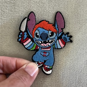 Può includere: Toppa ricamata raffigurante un personaggio dei cartoni animati blu con grandi orecchie, un sorriso malizioso e capelli rossi. Il personaggio indossa una tuta blu e tiene in mano un coltello. La toppa ha un bordo nero e accenti colorati.