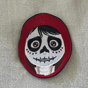 Miguel patch from Coco with painted skull face & red hoodie. 3.5x2.75 inch embroidered iron-on — perfect Disney Día de los Muertos accent.