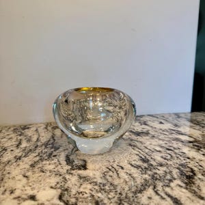May include: A clear, round glass bowl with a slightly flared base. The bowl has a golden rim and a textured interior. The bowl is sitting on a speckled countertop.