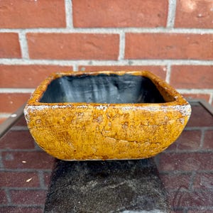 May include: A square, yellow ceramic planter with a distressed finish. The planter has a black interior and is perfect for small plants or succulents.