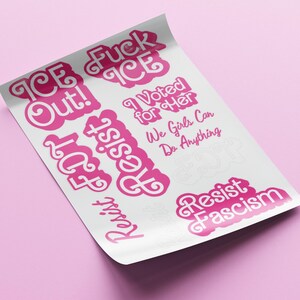 Op de afbeelding: Een vel stickers met roze tekst op een witte achtergrond. De stickers bevatten zinnen als "ICE Out!", "Resist", "I Voted for Her" en "Resist Fascism". Het vel is licht gekruld, tegen een roze achtergrond.