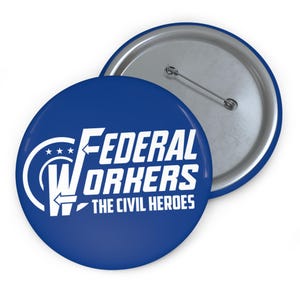 May include: Two round blue buttons with a silver pin backing. The front button has white text that reads "FEDERAL WORKERS THE CIVIL HEROES" with a graphic. The second button is partially visible.