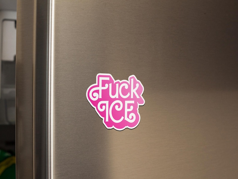 May include: A pink and white sticker with the words "Fuck ICE" in a stylized font. The sticker is affixed to a stainless steel refrigerator door. The sticker has a white border.