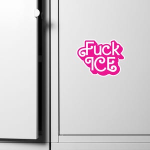 May include: A bright pink sticker with the words "Fuck ICE" in a stylized font. The sticker is affixed to a white surface, likely a refrigerator or cabinet door. The text is outlined in white.