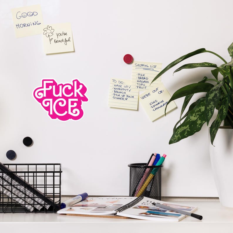 May include: A bright pink sticker with the words "Fuck Ice" in a stylized font. The sticker is on a white surface, with other sticky notes and office supplies visible in the background.