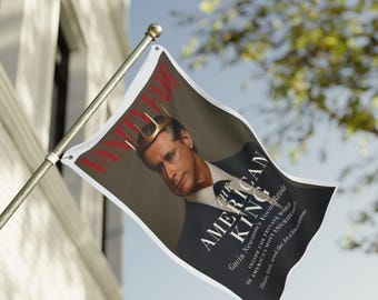 May include: A flag featuring a magazine cover with the text "Vanity Fair" in red. The cover image is of a man wearing a gold crown, with the title "The American King" and text about Gavin Newsom. The flag is white with a metal pole.