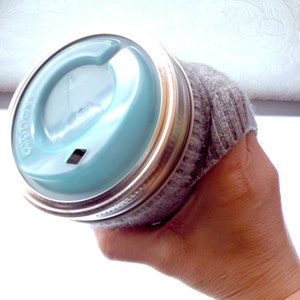 Op de afbeelding: Een glazen pot met een blauwe deksel en een grijze sok eromheen gewikkeld. De pot wordt vastgehouden door een hand.