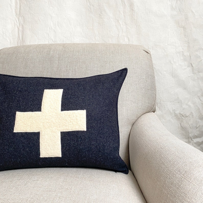 Puede incluir: Un coj&iacute;n de sof&aacute; negro y blanco con un gran signo m&aacute;s blanco sobre un sill&oacute;n beige.