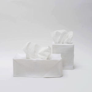 May include: Two white linen tissue box covers. The covers are square and have a textured surface. The tissue boxes are empty.