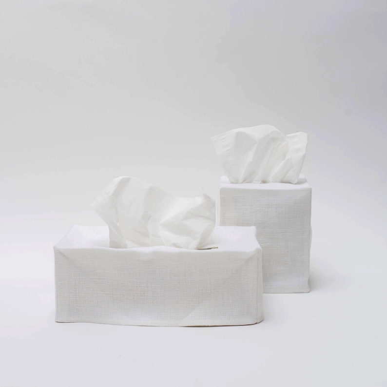 May include: Two white linen tissue box covers. The covers are square and have a textured surface. The tissue boxes are empty.