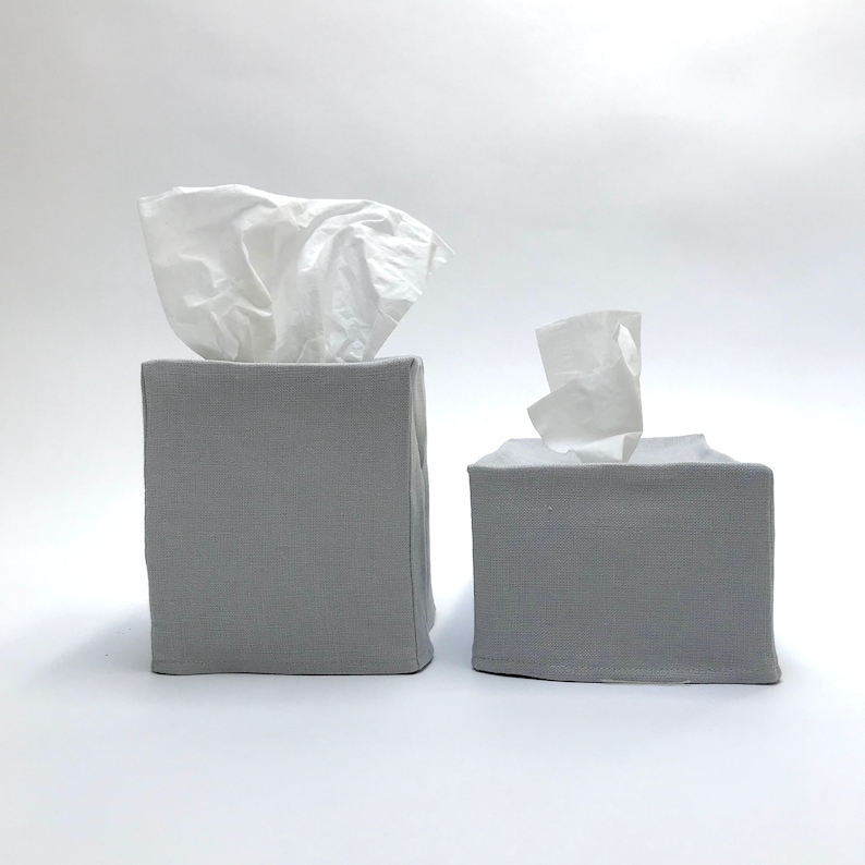 May include: Two gray linen tissue box covers. The larger cover has a white tissue box inside. The smaller cover has a white tissue box inside.