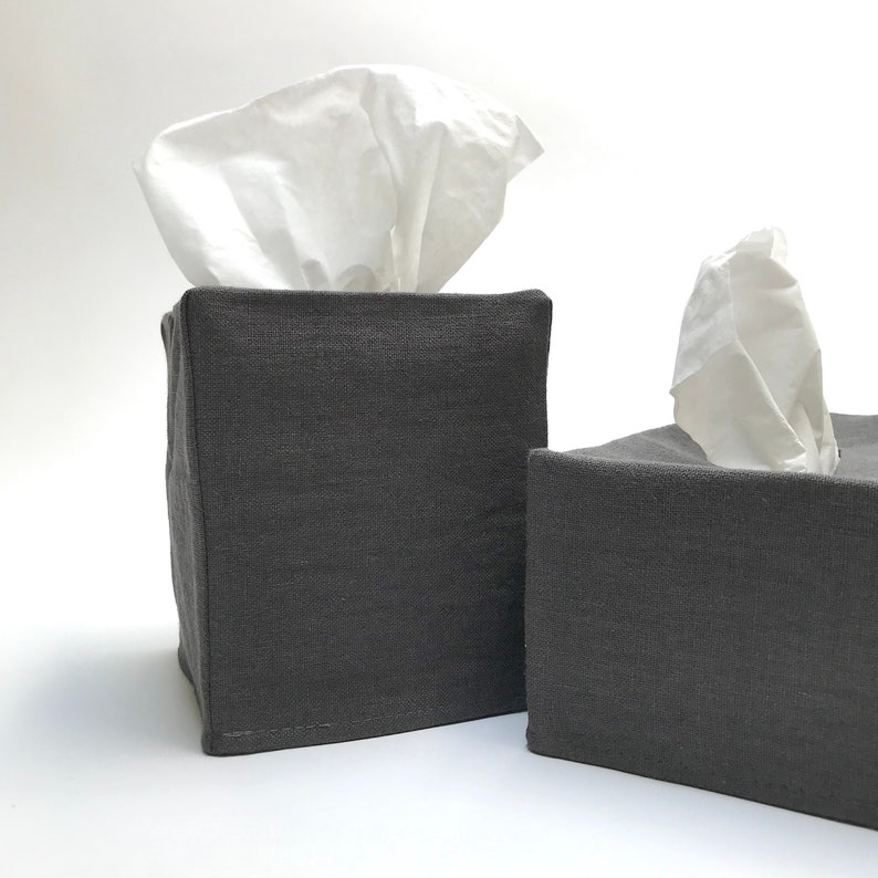 May include: Two gray linen tissue box covers. The tissue boxes are square and have a simple design.