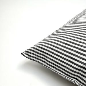 Puede incluir: Una esquina de una almohada con un patr&oacute;n de rayas blancas y negras. Las rayas est&aacute;n espaciadas uniformemente y corren diagonalmente por la almohada. La almohada est&aacute; sobre un fondo blanco.