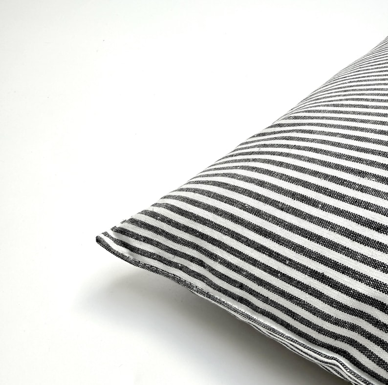 Puede incluir: Una esquina de una almohada con un patr&oacute;n de rayas blancas y negras. Las rayas est&aacute;n espaciadas uniformemente y corren diagonalmente por la almohada. La almohada est&aacute; sobre un fondo blanco.