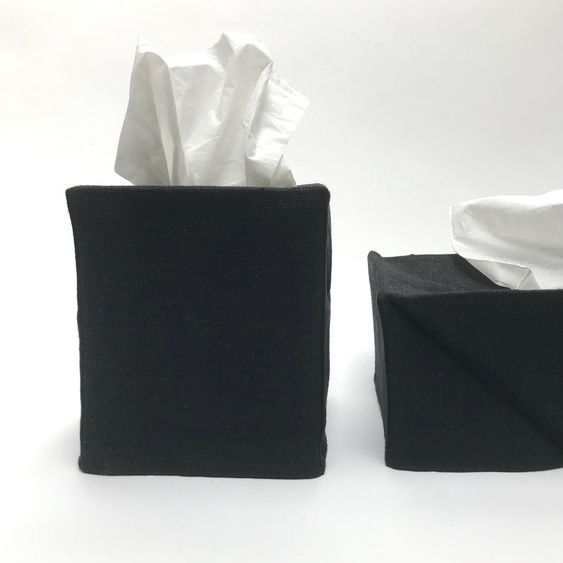 May include: Two black fabric tissue box covers. The covers are square and have a simple design. The tissue boxes are filled with white tissues.