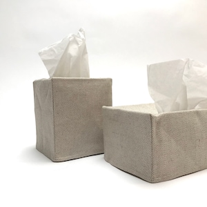 May include: Two beige linen tissue box covers with white tissues inside. The covers are square and have a subtle texture.