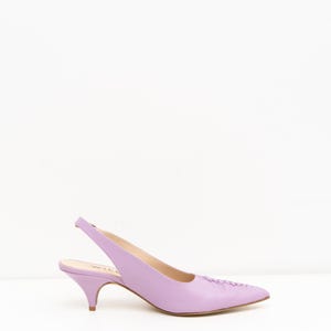 May include: A lavender slingback pump with a pointed toe and a low kitten heel. The shoe features a smooth finish, a delicate strap wrapping around the heel, and a subtle stitched detail along the top of the toe box for a clean, structured look.