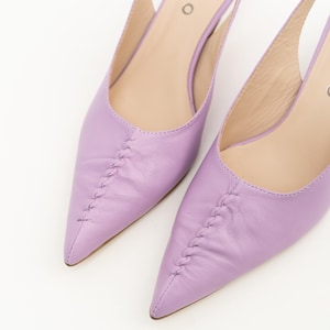 May include: A pair of lavender pointed-toe slingback heels with a central braided seam detail on the vamp. The interior insole features the brand name WILLO printed in black. The shoes have a smooth finish and a structured slingback strap design.