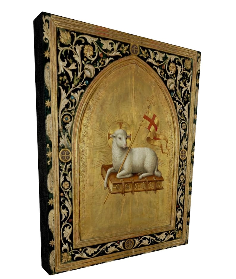May include: A framed religious artwork featuring a lamb holding a flag with a cross. The lamb rests on a book within a gold arched frame. The frame has a black border with floral and leaf designs.
