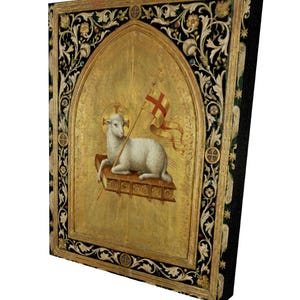May include: A religious artwork featuring a lamb holding a flag with a cross, set against a gold background. The artwork is framed with ornate black and gold floral designs. The lamb is white, and the flag is red and white.