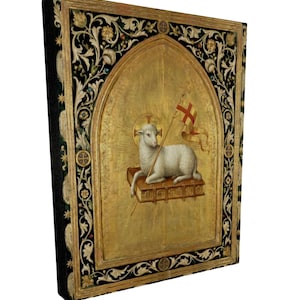 May include: A framed religious artwork featuring a lamb holding a flag with a cross. The lamb is resting on a book, set against a gold background. The frame has ornate floral and geometric designs in black and gold.