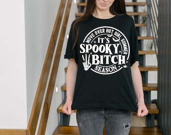 May include: A black t-shirt with a white circle graphic that says "Move Over Hot Girl Summer It's Spooky Bitch Season". The graphic also includes a skeleton hand making a peace sign and a spider.
