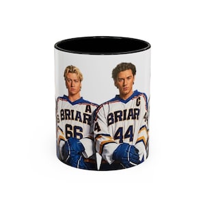 Puede incluir: Una taza de café de cerámica blanca con interior negro. La taza presenta un diseño de dos hombres con camisetas de hockey con la palabra "Briar" y los números 66 y 44. Las camisetas son blancas, azules y doradas.