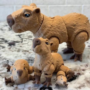 May include: A family of brown capybara figurines. The largest capybara stands upright, while the others are in various poses. The figurines have detailed features, including textured fur and realistic facial expressions. The smallest capybara is lying down.