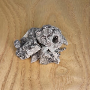 May include: A pile of irregularly shaped, dark gray and black objects with a white, powdery coating. The objects are clustered together on a light brown, wood-grain surface. Some pieces have holes.